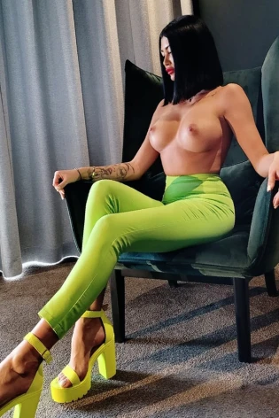 Milan sitting down while topless and showing off her green pants 